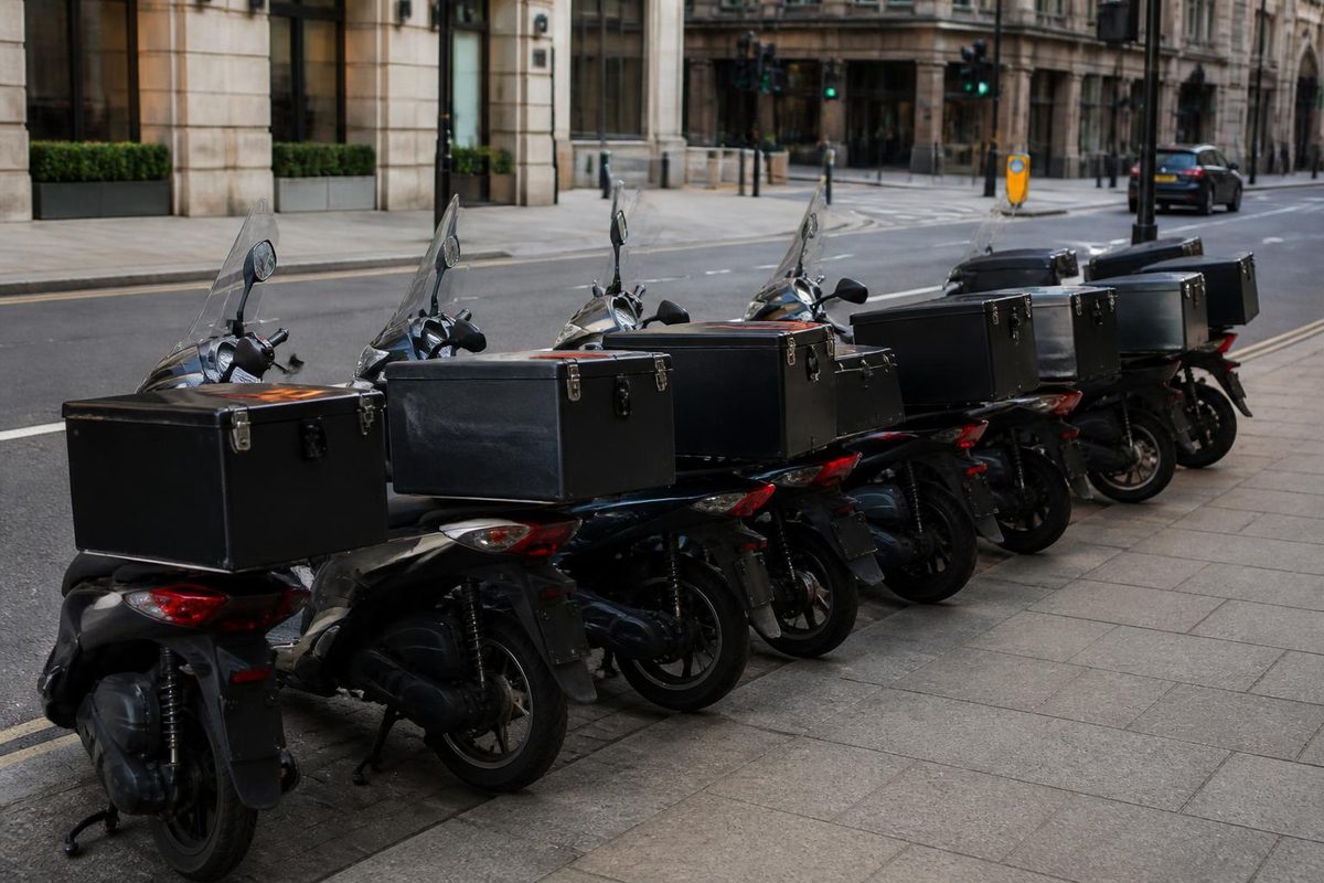 Row of delivery scooters with top boxes parked on a city street