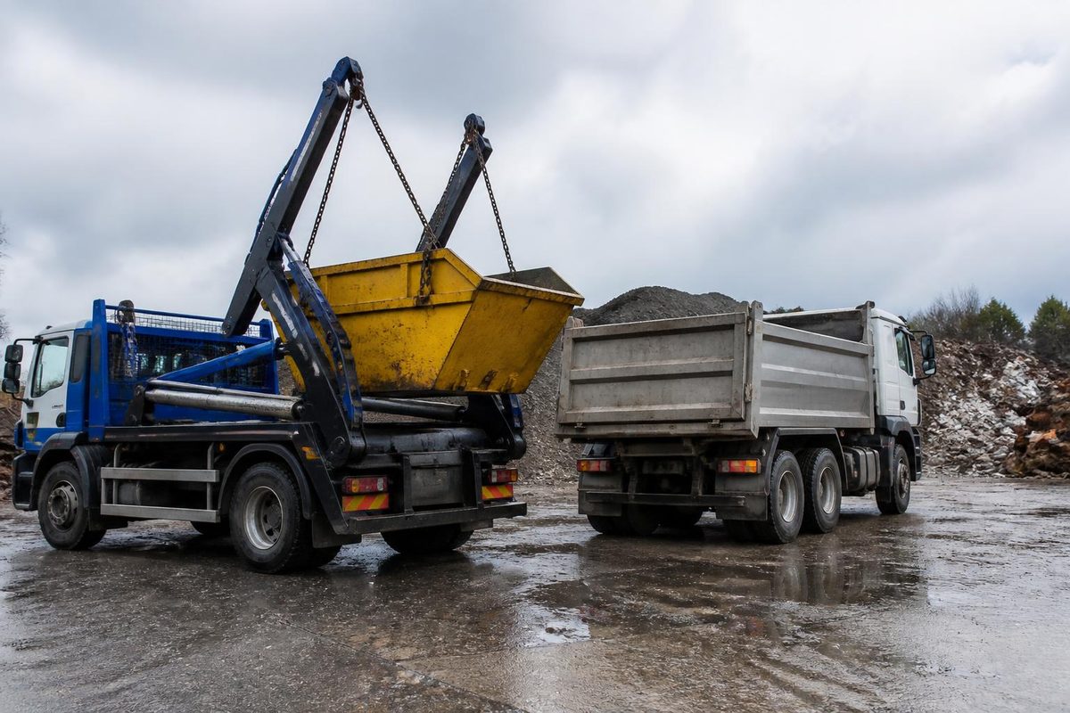 Skip loader lorry lowering a yellow skip onto a residential driveway